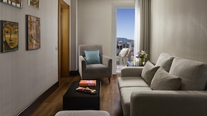 Una sala moderna con sofá, sillón y mesa de centro. Hay obras de arte enmarcadas en la pared y vistas de la ciudad a través de un ventanal grande.