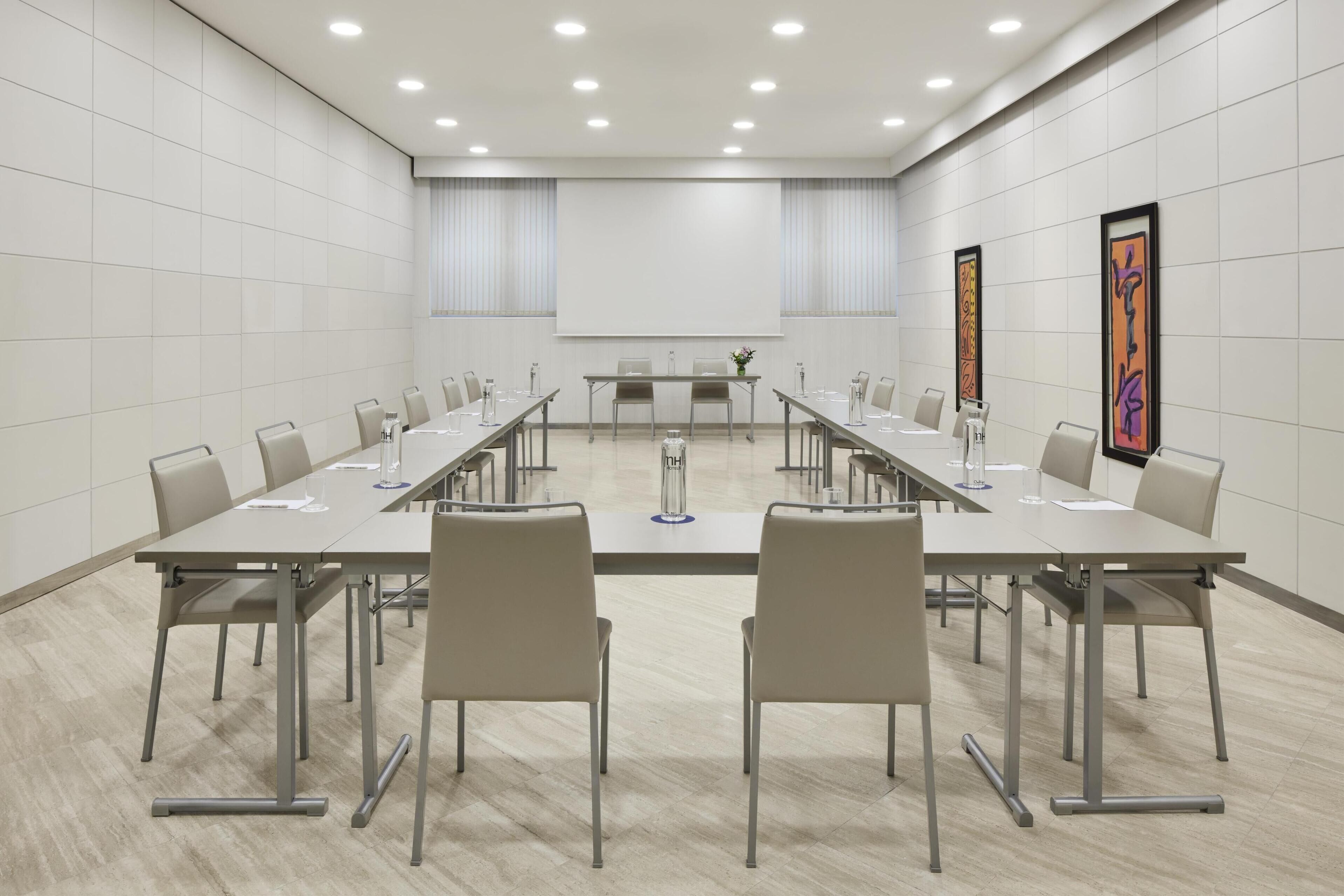 Une salle de conférence avec une longue table, des chaises, un écran de projection et des œuvres d’art encadrées accrochées aux murs.