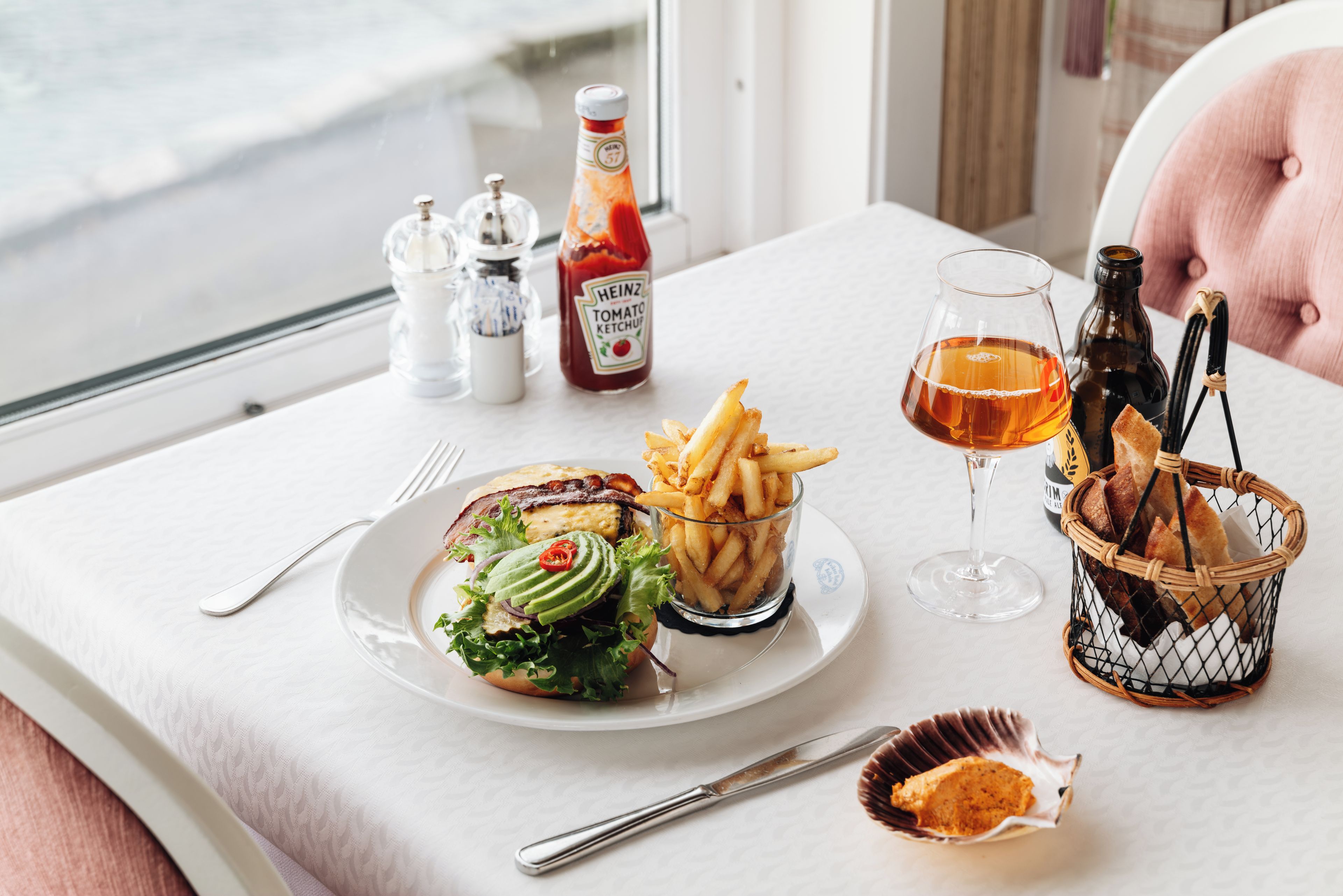 A table with a burger, fries, a glass of beer, and condiments.