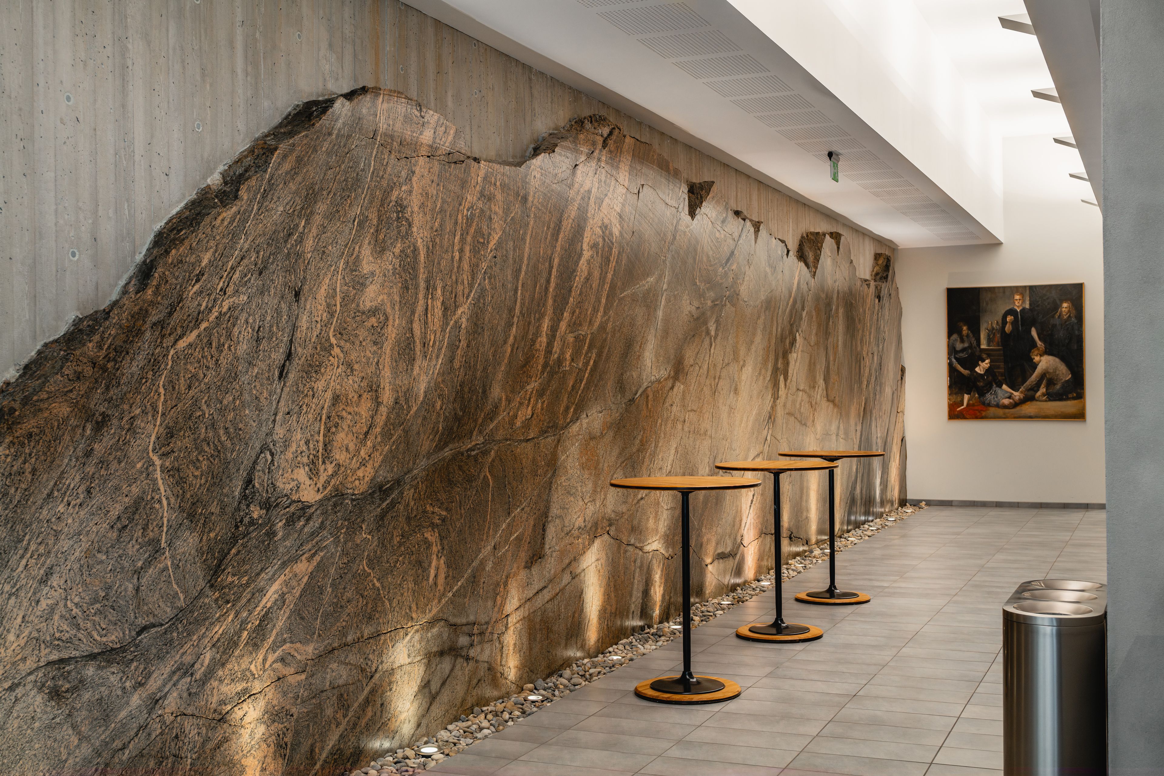 A modern interior with a large stone wall, minimalist tables, and a painting on the wall.