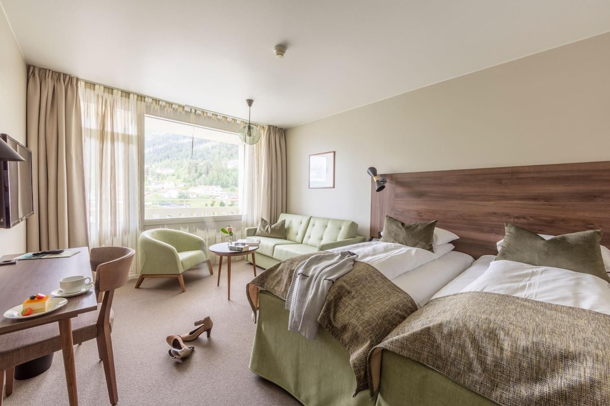 A hotel room with a bed, a desk, a chair, a small table, and a window with curtains.