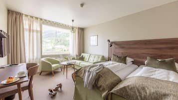 A hotel room with a bed, a desk, a chair, a small table, and a window with curtains.