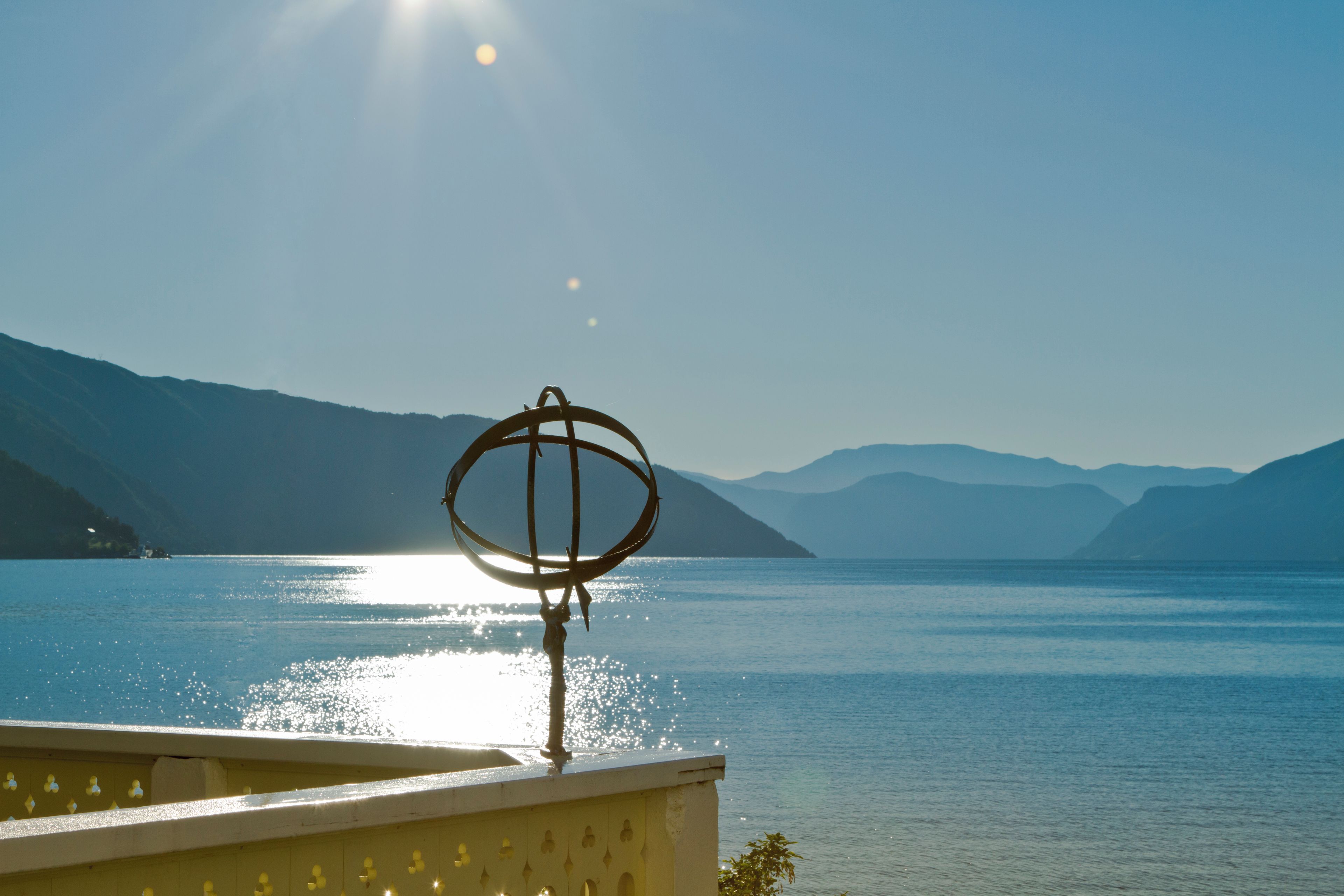A lake with mountains in the background and a sun reflecting on the water.