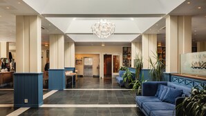 A hotel lobby with a high ceiling, a central chandelier, seating areas, and a reception desk.
