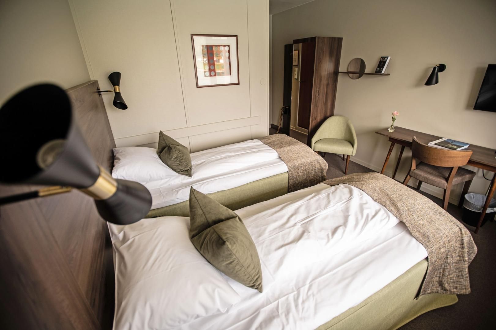 Habitación de hotel con dos camas, un escritorio, una silla, un armario y un televisor montado en la pared.
