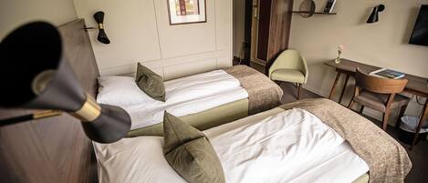 Habitación de hotel con dos camas, un escritorio, una silla, un armario y un televisor montado en la pared.