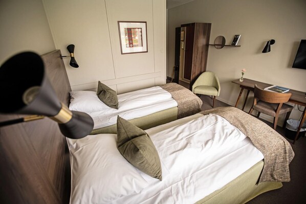 A hotel room with two beds, a desk, a chair, a wardrobe, and a wall-mounted TV. - Kviknes (Sogndal)