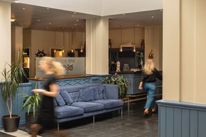 Eine Hotelhalle mit einem blauen Sofa, Zimmerpflanzen, einer Bar und einer Schiffslaugensäge als Dekoration.