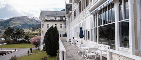 A building with a balcony, outdoor seating, and a view of a mountainous landscape.