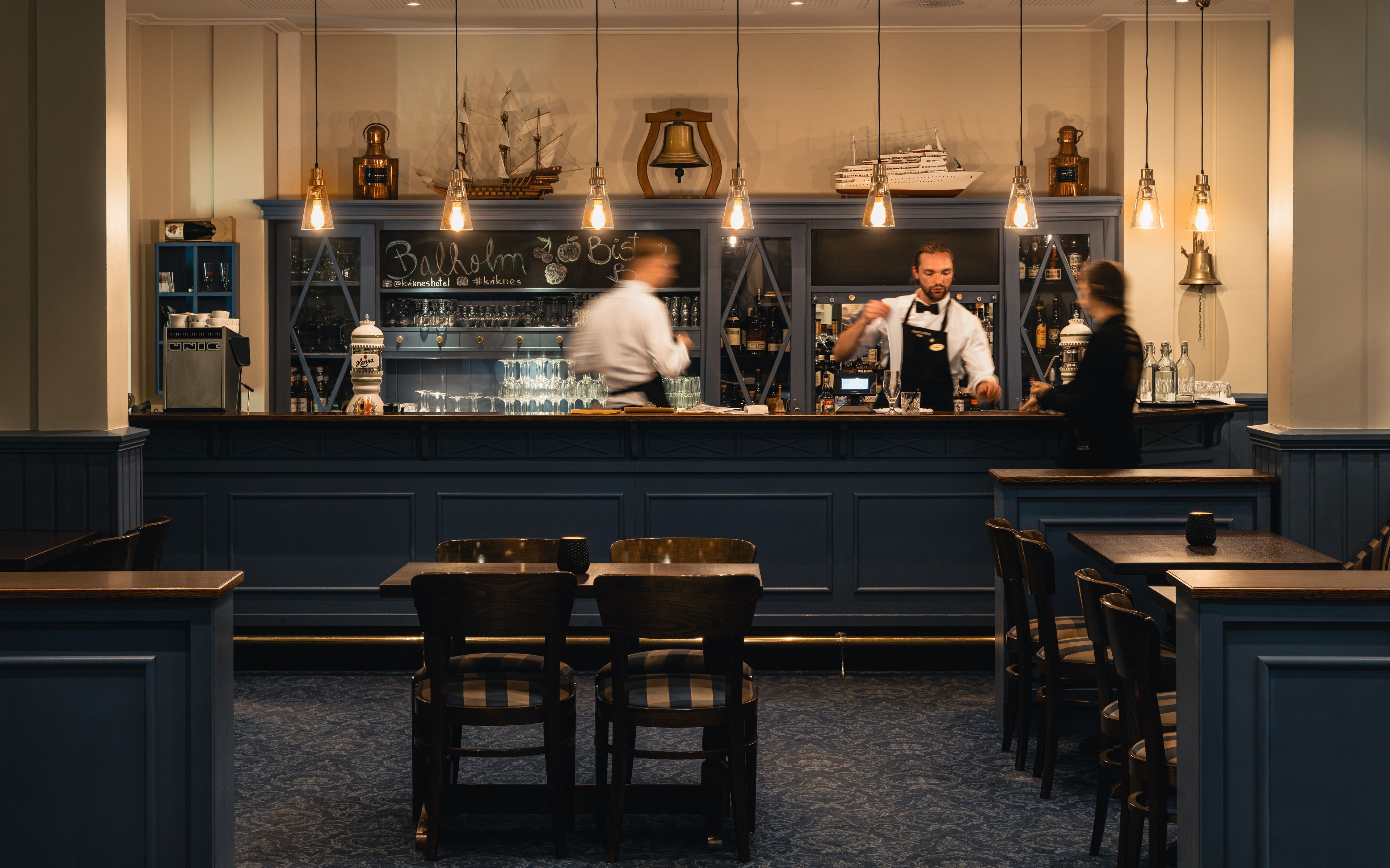 Un espace bar comprenant un comptoir, des tabourets de bar et un coin salon avec des tables et des chaises.