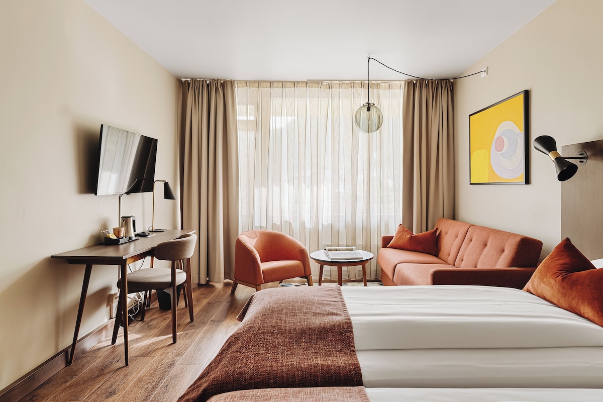A hotel room with a bed, a desk, a chair, a sofa, and a TV.