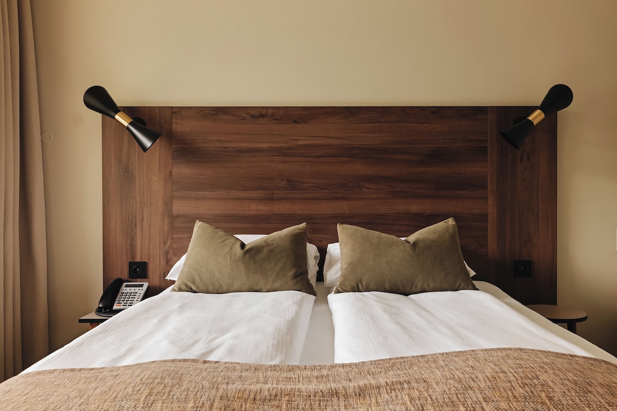 A double bed with two pillows, a wooden headboard, bedside tables with lamps, and a telephone on a nightstand.