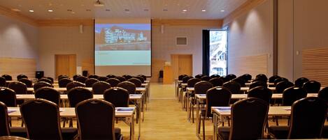 A conference room with rows of chairs and tables, a large screen at the front, and a projection screen on the right.