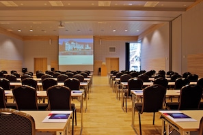 A conference room with rows of chairs and tables, a large screen at the front, and a projection screen on the right.