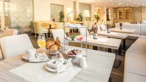 A modern dining area with a three-tiered breakfast tray, white chairs, and a clean, contemporary design. - Am Neutor Hotel Salzburg Zentrum (Salzburg)
