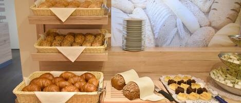 Una vitrina de panadería con diversos tipos de pan y pasteles, incluyendo croissants y panes redondos, dispuestos en estantes de madera y una tabla de cortar.