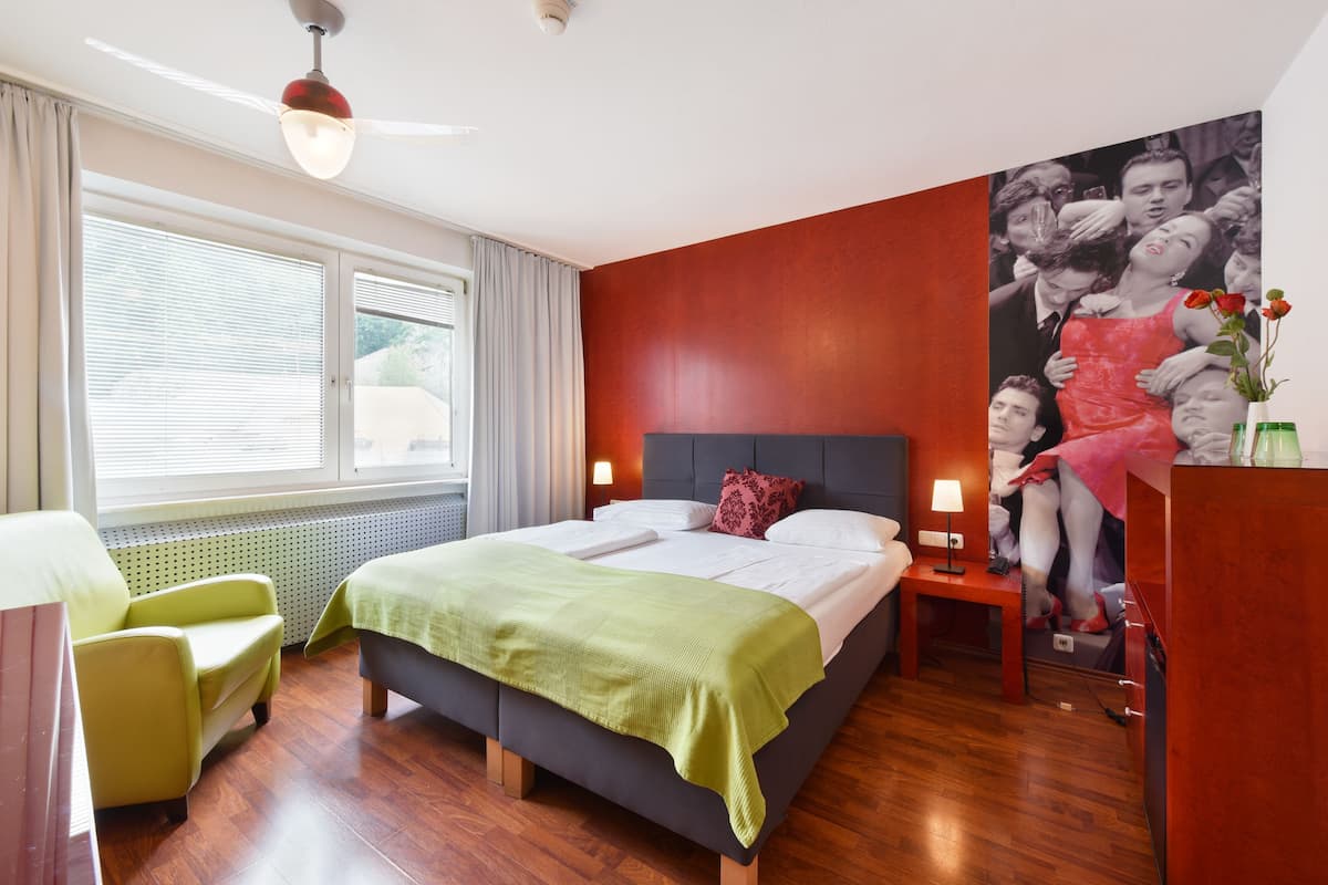 A hotel room with a bed, a chair, a desk, a lamp, and a window with curtains.