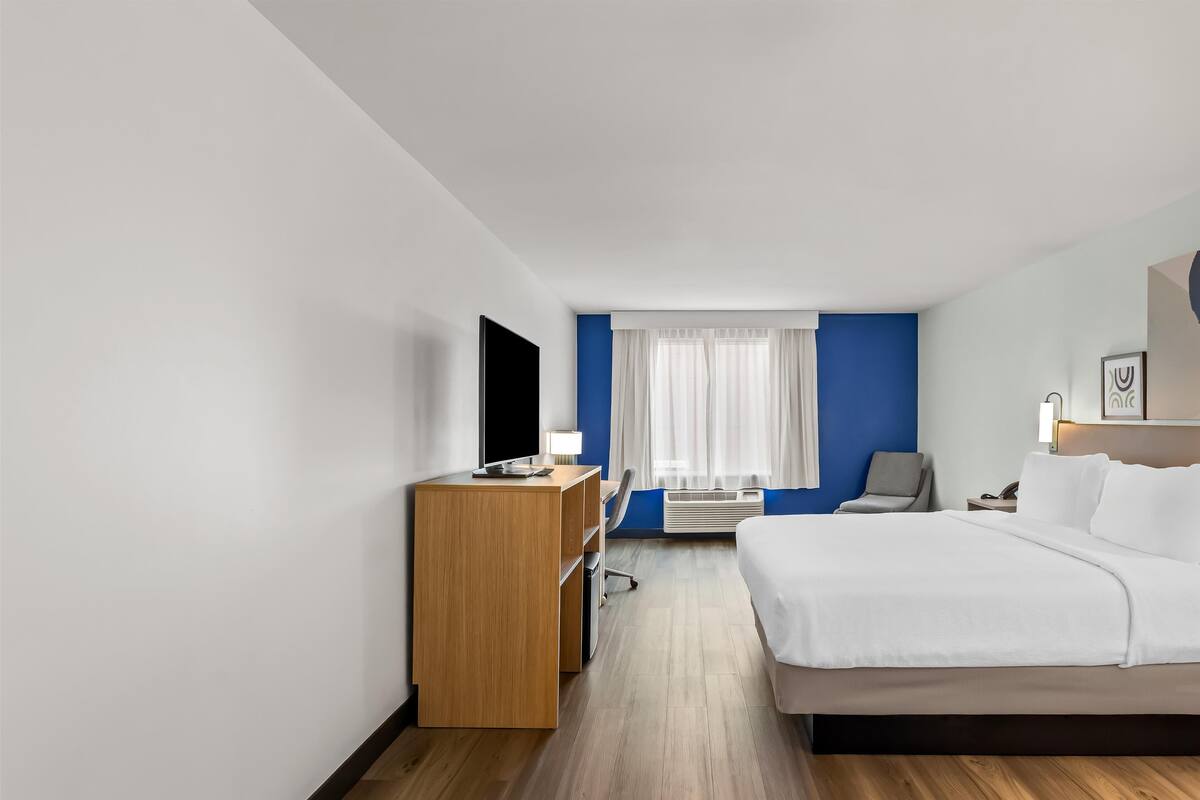 Una habitación de hotel con cama, escritorio, silla, televisión y ventana con cortinas.