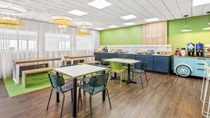 A modern cafe with wooden tables, green chairs, and a green accent wall.