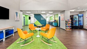 A modern lobby with a green carpet, orange rocking chairs, a white table, and a vending machine.