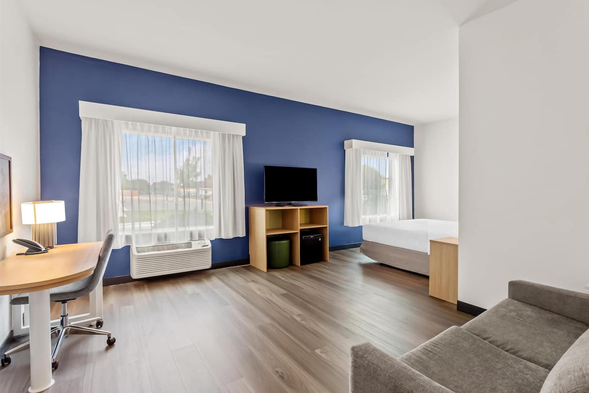 Habitación de hotel con cama, escritorio con silla, televisor y ventana con cortinas.