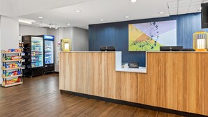 A hotel reception area with a wooden reception desk, a large digital screen, and a vending machine.