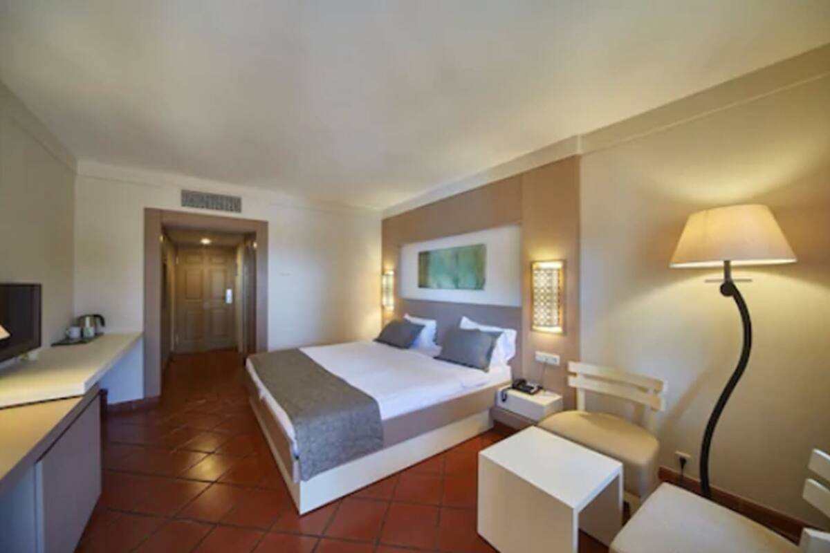 A hotel room with a bed, bedside table, lamp, and a small desk with a chair.