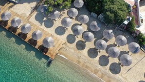 An aerial view of a beach with rows of umbrellas and lounge chairs, a wooden deck, and clear turquoise water. - Hapimag Resort Sea Garden (Bodrum)