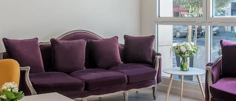 A modern living room with a purple sofa, yellow chairs, a white table, and large windows offering a view of the street.