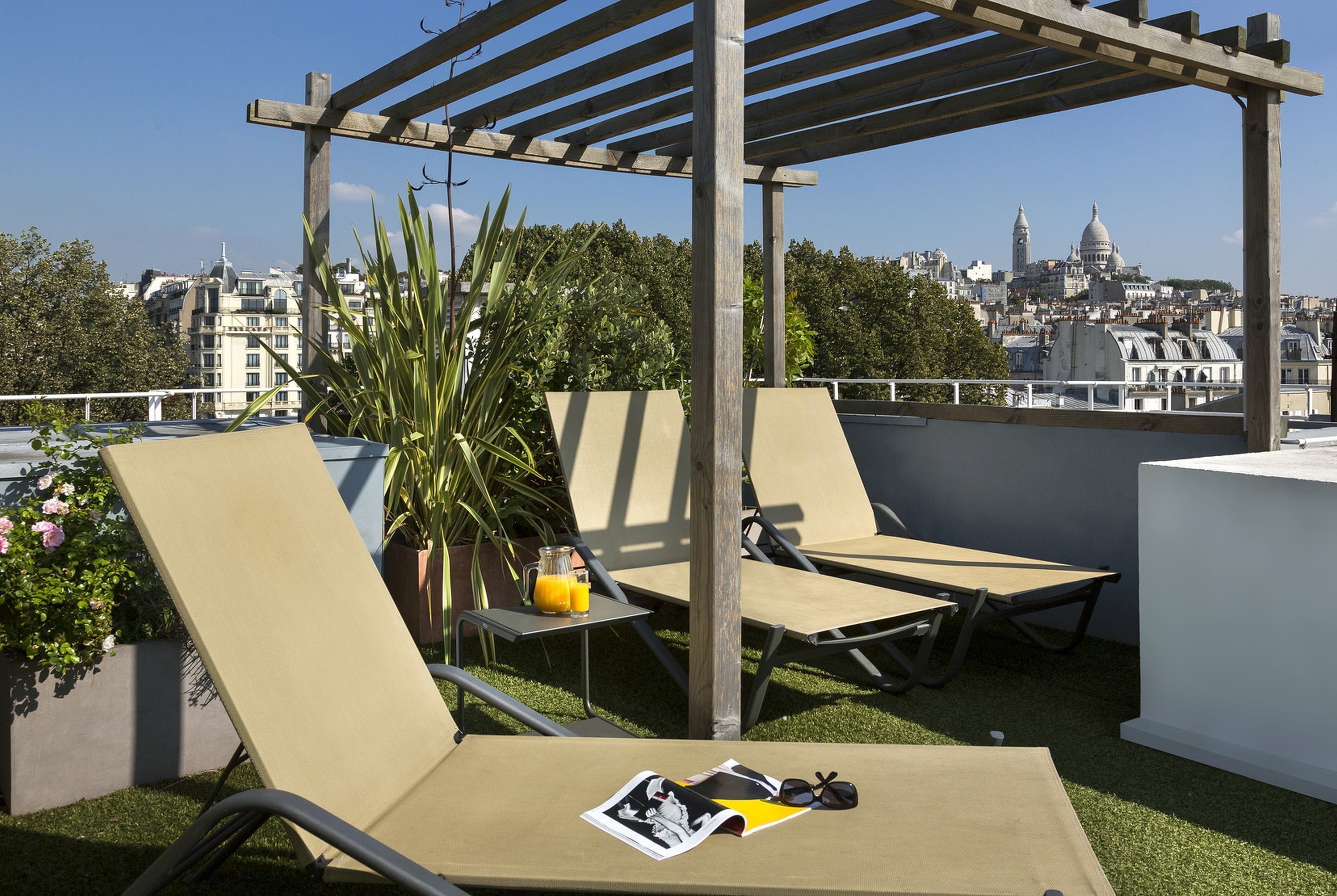 A rooftop terrace with two lounge chairs, a wooden pergola, and a view of a cityscape with domed buildings.