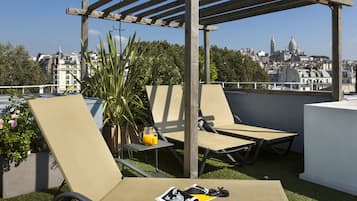 Una terraza en la azotea con dos sillones, una pérgola de madera y vistas a un paisaje urbano con edificios de cúpulas.