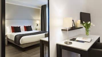 A hotel room with a bed, bedside table, lamp, and a small desk with a chair.