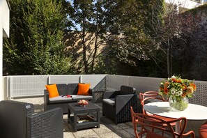 Relax on the patio with a sofa, armchairs, and a small table, surrounded by lush greenery.