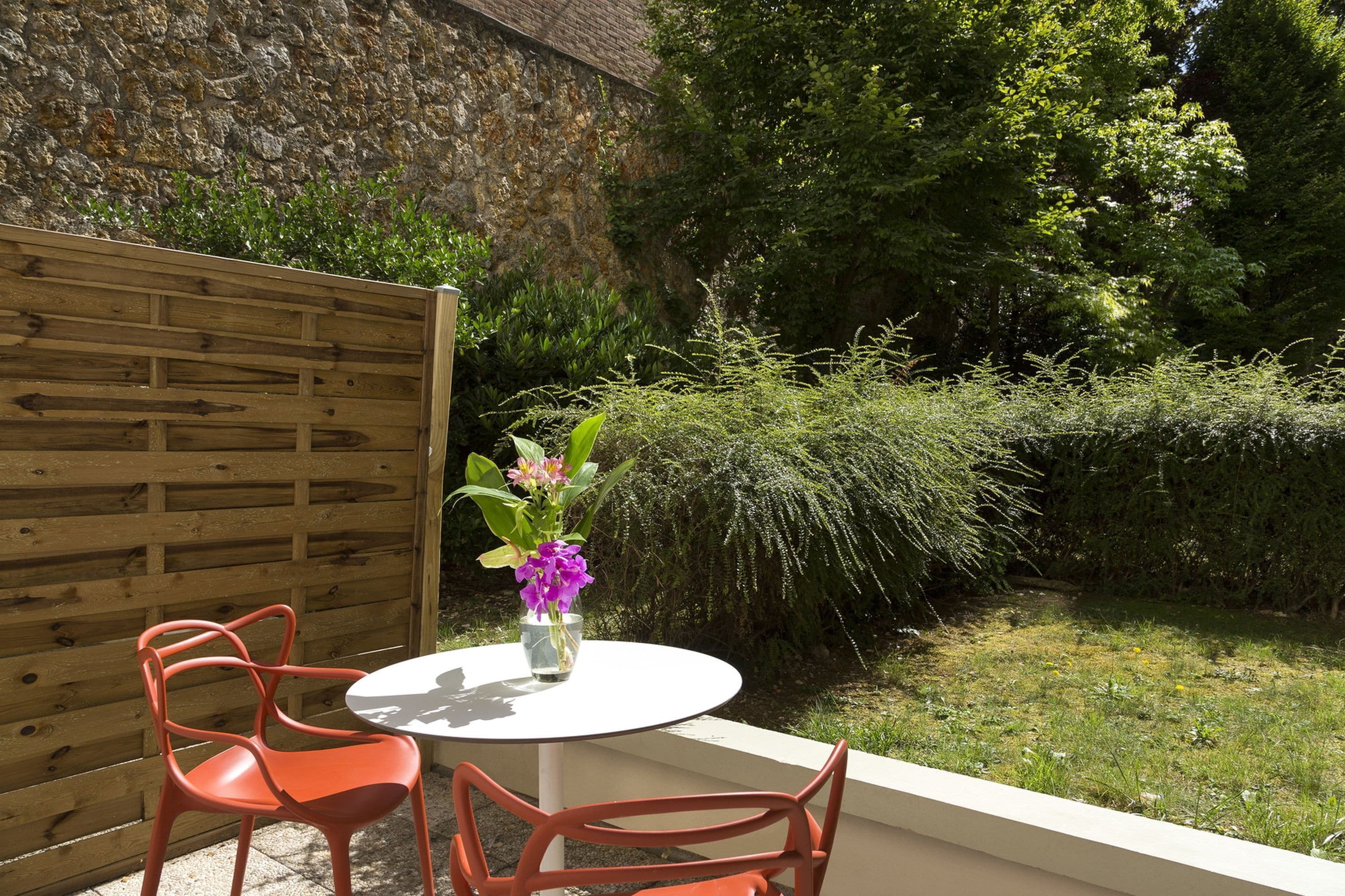 A small outdoor patio with a round table and two chairs, a wooden fence, and a stone wall in the background.