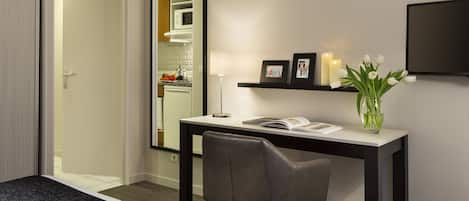 A modern room with a desk, chair, and a mirror. There is a TV mounted on the wall, a vase with flowers, and a picture frame.