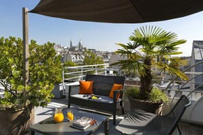 Enjoy breathtaking views of the historic cityscape from this rooftop terrace, featuring a wicker sofa, chair, and table.