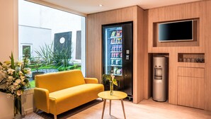 A modern hotel room with a yellow sofa, a small round table, a refrigerator, a water dispenser, and a TV mounted on the wall. - Citadines Montmartre Paris (Paris)