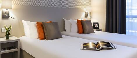A modern hotel room with two beds, a geometric-patterned wall, bedside lamps, and a view of the city through large windows.