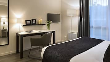 Une chambre d’hôtel comprenant un lit, un bureau avec une chaise, une télévision, une lampe et une fenêtre avec des rideaux.
