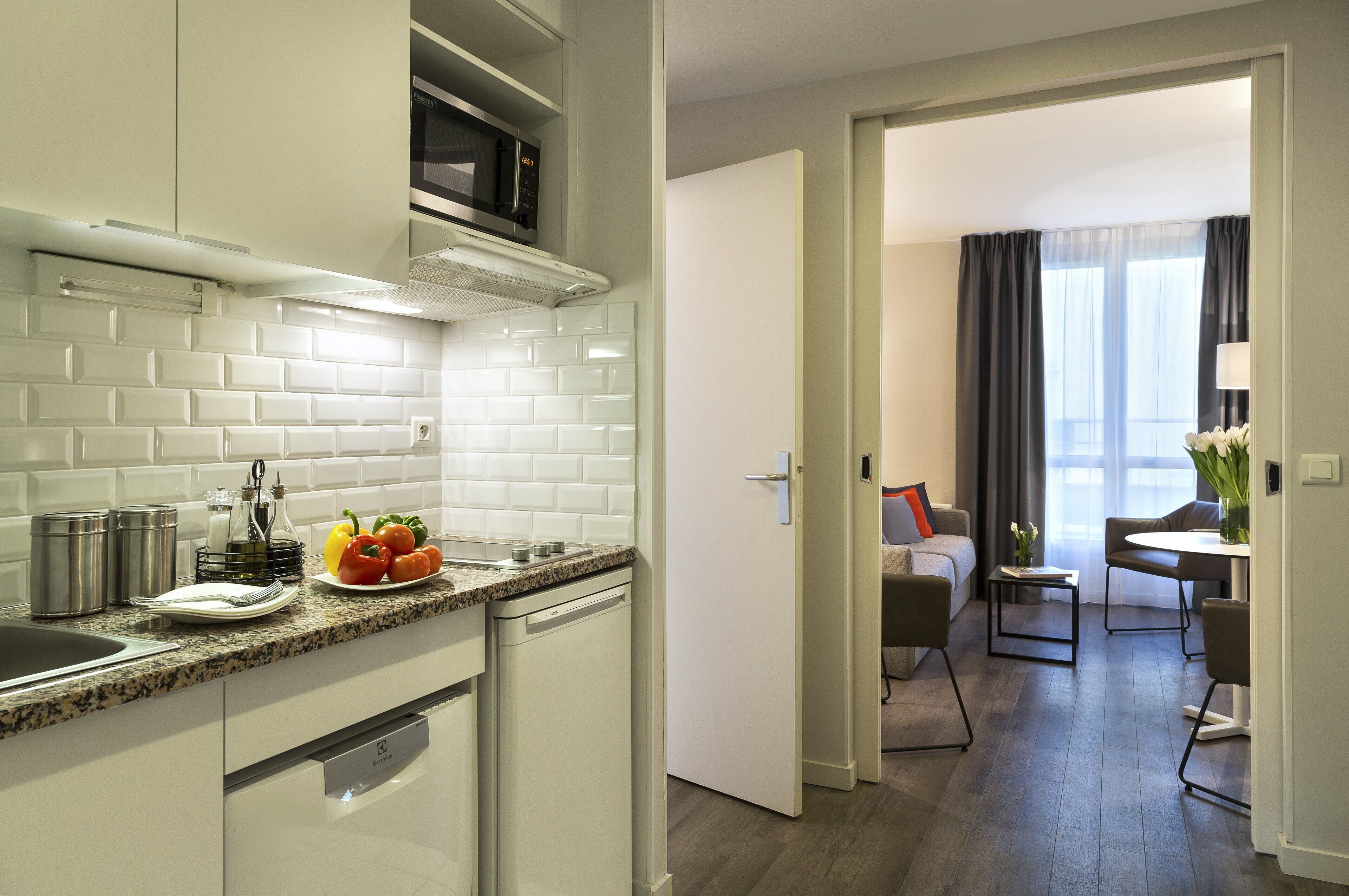 A modern kitchen with white cabinets, a granite countertop, and a microwave. There is a dining area with a table and chairs visible through an open door.
