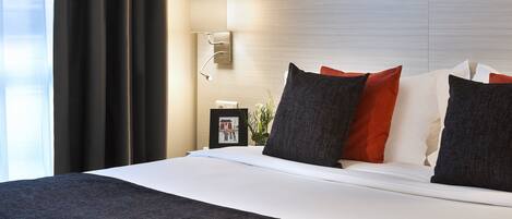 Un hotel moderno con una cama grande, una mesita de noche con lámpara y vistas al exterior a través de cortinas translúcidas.