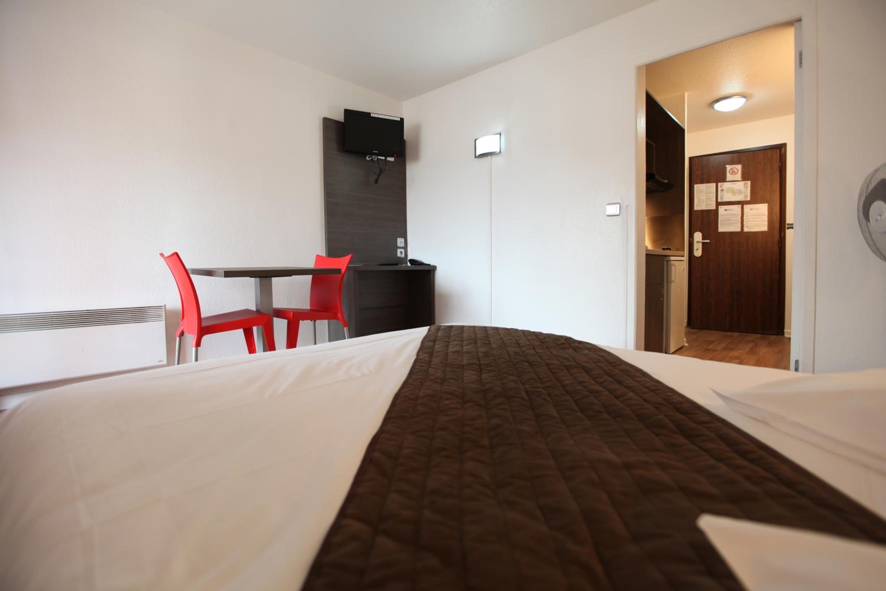 A hotel room with a bed, a desk, a chair, and a TV mounted on the wall.