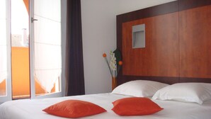 Ein Hotelzimmer mit einem großen Bett, weißer Bettwäsche und zwei orangefarbenen Kissen.