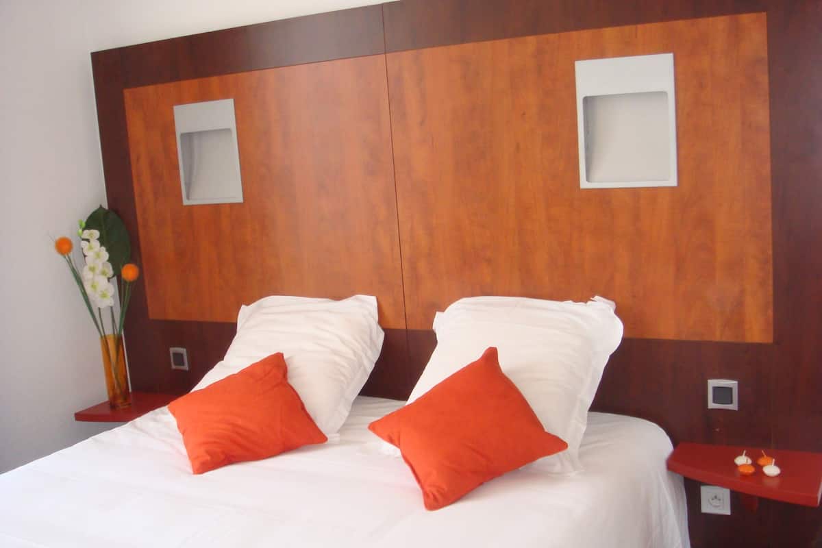 A hotel room with a wooden headboard, two white pillows, and two orange pillows.