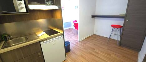 Uma cozinha compacta com lava-louças, micro-ondas e pia. Existe uma cadeira vermelha e um banquinho na área de jantar adjacente.