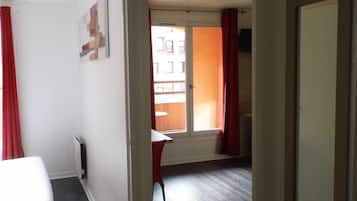 Una habitación con cama, escritorio y ventana con cortinas rojas.