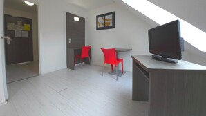 Ein Zimmer mit schrägem Dach, einem Fernseher auf einem Holzboden, zwei roten Stühlen und einem kleinen Tisch.