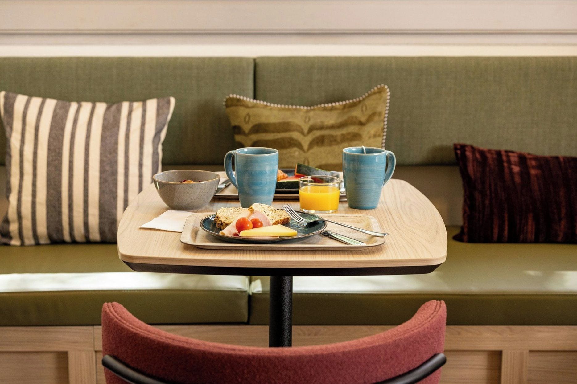 A breakfast setup on a wooden table with a tray, a bowl, two mugs, and a glass of orange juice.