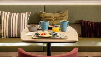 A breakfast setup on a wooden table with a tray, a bowl, two mugs, and a glass of orange juice.