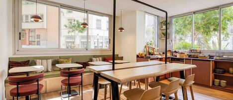 Un café moderno con una larga mesa de madera, sillas rojas y una zona de estar con un banco.